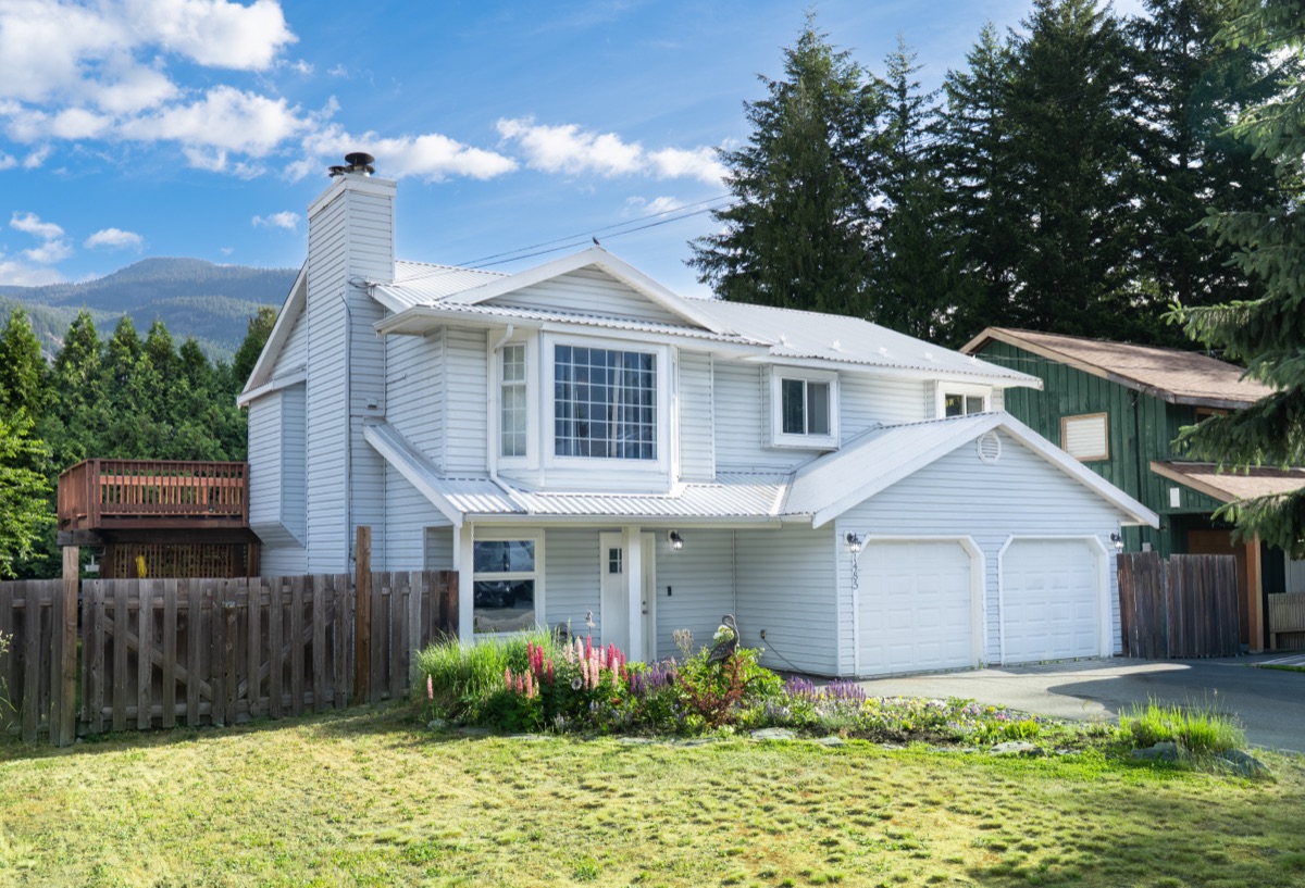 Two-storey home with a double garage, flower garden and mountains behind